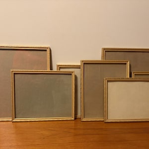 Puede incluir: Una colección de ocho marcos de fotos rectangulares con bordes de madera fina y clara. Los marcos varían en tamaño y orientación, presentando configuraciones tanto verticales como horizontales, dispuestos en grupo con frentes de cristal.