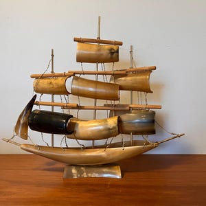 May include: A decorative ship sculpture made of polished horn and wood. The ship has multiple sails and a wooden mast. The ship is mounted on a horn base.