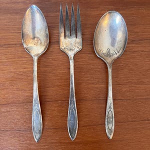 Pode incluir: Três peças de talheres vintage: um garfo, uma colher e uma colher de servir. Todos são prateados e têm desenhos ornamentados.