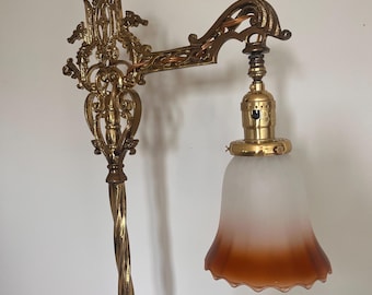 Puede incluir: Una lámpara de pie antigua de latón con un diseño ornamental y en espiral. La lámpara presenta un poste retorcido y un brazo curvo que sostiene una pantalla de vidrio esmerilado con un efecto degradado, que pasa de blanco a ámbar. La lámpara es una pieza vintage.