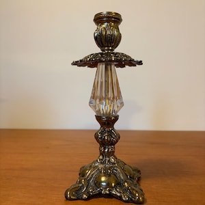 May include: An antique brass candlestick holder with a clear, faceted crystal center. The base and top are ornate with floral and scroll details. The candlestick is approximately 8 inches tall.