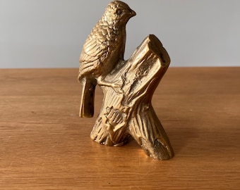May include: A gold-colored metal sculpture of a bird perched on a tree branch.