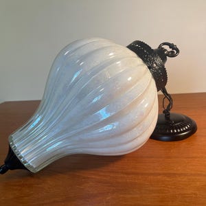 May include: A white glass pendant light with a ribbed design. It features a black metal cap and base. The light fitting is designed for ceiling suspension and is suitable for indoor lighting. The dimensions are in centimetres.