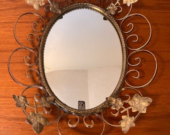 May include: A gold-toned oval mirror with a decorative frame made of swirling metal and leaf accents.