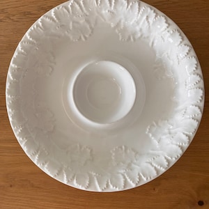 May include: White ceramic serving dish with a smaller bowl in the center. The dish has a raised leaf design around the edge.