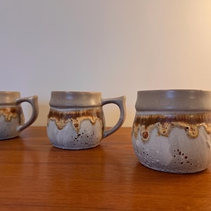 May include: Three ceramic mugs with a brown and white speckled glaze. The mugs have a rounded shape and a handle.