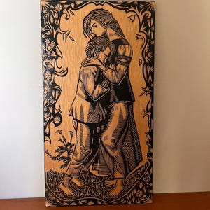 May include: Black and white woodblock print of a woman embracing a child. The print is framed with a decorative border of flowers and leaves.
