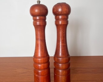 Può includere: Un set di due saliere e pepiere in legno con una finitura marrone rossiccia. Le saliere hanno una parte superiore rotonda e un corpo cilindrico con un design scanalato.