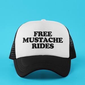 May include: White trucker hat with black mesh back and black brim. The hat has the text "FREE MUSTACHE RIDES" printed in black.