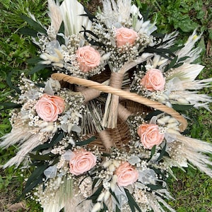K&ouml;nnte beinhalten: Ein Weidenkorb gef&uuml;llt mit pfirsichfarbenen Rosen, wei&szlig;em Schleierkraut und getrocknetem Pampasgras. Das Arrangement umfasst dunkelgr&uuml;ne Bl&auml;tter und ist auf gr&uuml;nem Gras platziert. Der Korb hat einen geflochtenen Griff.