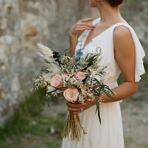 Medium size free form salmon rose bridal bouquet with preserved roses, pampas grass, eucalyptus and gypsophila, held by bride at sunset — elegant boho rustic dried wedding flowers handmade by GulFloraWedding.