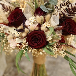 May include: A burgundy and cream dried flower bouquet with burgundy roses, white baby's breath, and dried grasses.