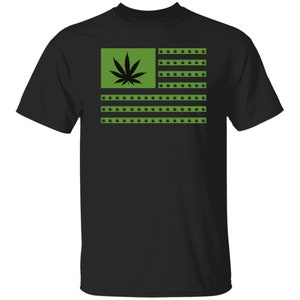 Op de afbeelding: Zwart T-shirt met een groen en zwart marihuanabladontwerp in de vorm van de Amerikaanse vlag.