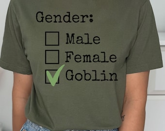 Könnte beinhalten: Ein grünes T-Shirt mit dem Text "Geschlecht:" und einer Checkliste mit den Optionen "Männlich", "Weiblich" und "Goblin". Die Option "Goblin" ist mit einem grünen Häkchen angekreuzt.