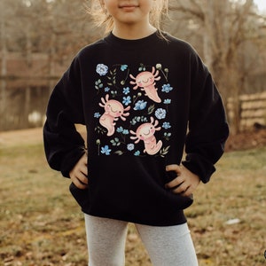 May include: A black sweatshirt with a graphic print of three pink axolotls with blue flowers and green leaves. The axolotls are smiling and have small, round bodies.