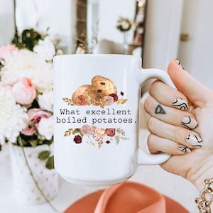 May include: White ceramic mug with a floral design and the text "What excellent boiled potatoes."