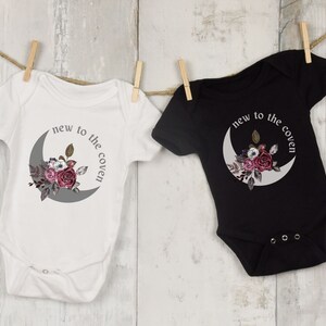 K&ouml;nnte beinhalten: Zwei Baby-Bodys, einer wei&szlig; und einer schwarz, mit einem Halbmond und einem Blumendesign. Der Text auf den Bodys lautet "new to the coven".
