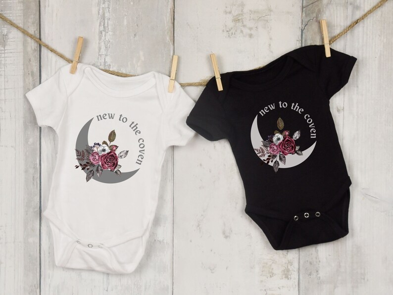 K&ouml;nnte beinhalten: Zwei Baby-Bodys, einer wei&szlig; und einer schwarz, mit einem Halbmond und einem Blumendesign. Der Text auf den Bodys lautet "new to the coven".