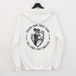 May include: White hooded sweatshirt with a black graphic print on the back. The graphic features a couple of skeletons in a heart with the text "From our first kiss till our last breath".