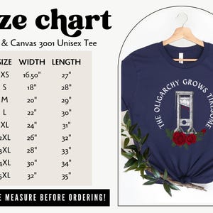 May include: Navy blue unisex t-shirt with the text "THE OLIGARCHY GROWS TIRESOME" and a guillotine graphic. A size chart is included, with measurements in inches. The shirt is hanging on a wooden hanger.