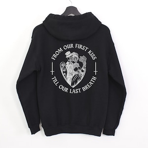 May include: Black hooded sweatshirt with a white graphic print of a couple of skeletons in a heart shape. The text around the heart reads "From our first kiss till our last breath."