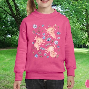 May include: Pink sweatshirt featuring a design of three axolotls and flowers. The axolotls are pink with black eyes. The flowers are blue and white.
