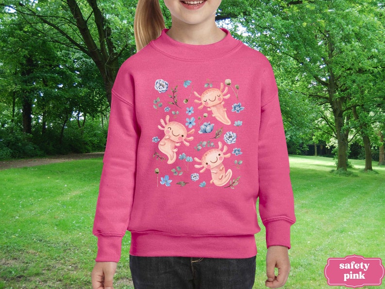 May include: Pink sweatshirt featuring a design of three axolotls and flowers. The axolotls are pink with black eyes. The flowers are blue and white.