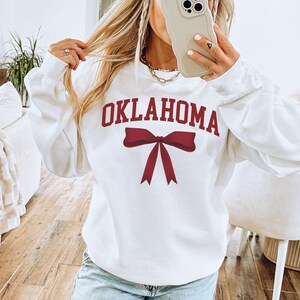 May include: White sweatshirt with a red bow and the word "OKLAHOMA" printed on the front.