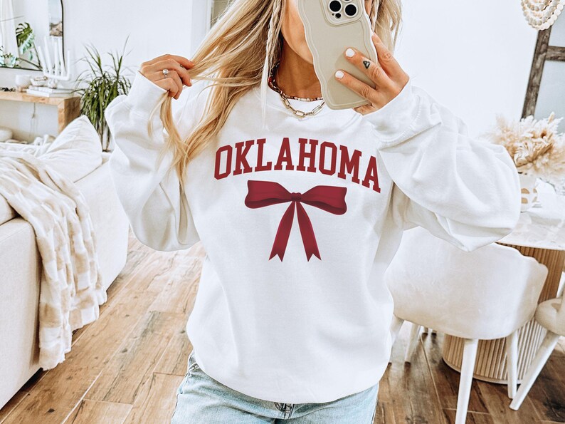 May include: White sweatshirt with a red bow and the word "OKLAHOMA" printed on the front.