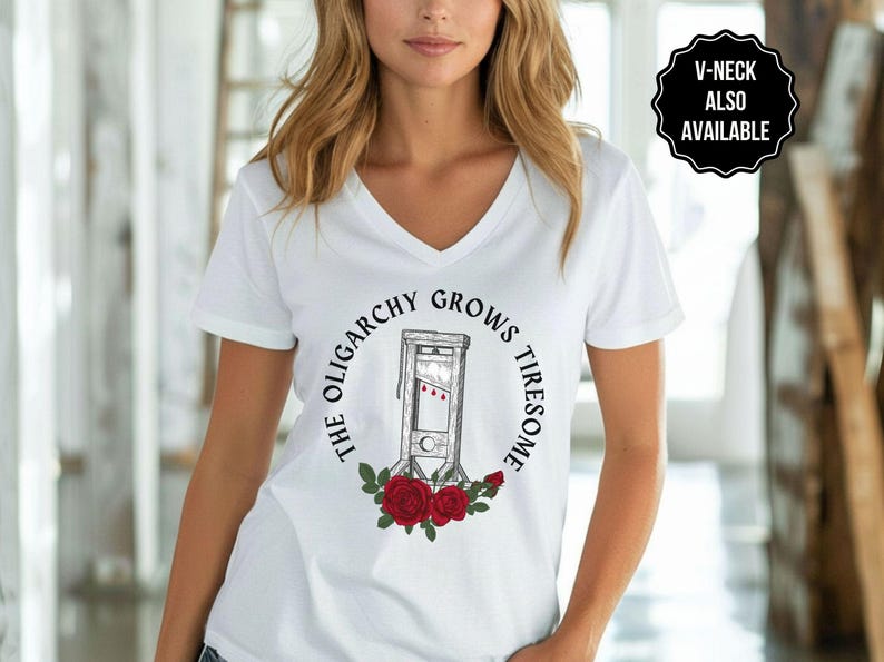 May include: White V-neck t-shirt featuring a graphic of a guillotine surrounded by the text "THE OLIGARCHY GROWS TIRESOME" and red roses. A black and white badge in the upper right corner says "V-NECK ALSO AVAILABLE".