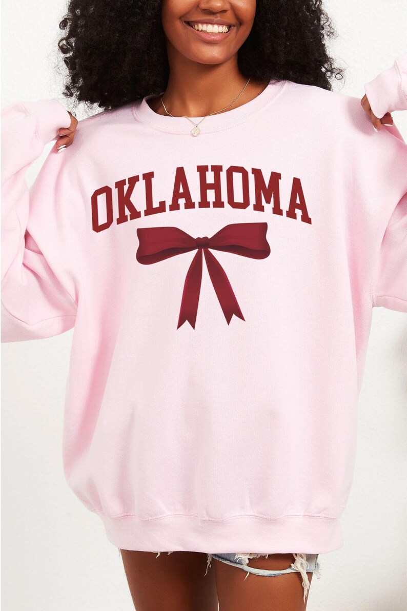 May include: Pink sweatshirt with the word "OKLAHOMA" in maroon letters and a maroon bow.