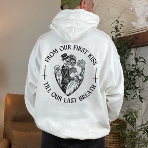May include: White hoodie with a black graphic print of two skeletons holding hands in a heart shape. The text around the graphic reads "From our first kiss till our last breath."