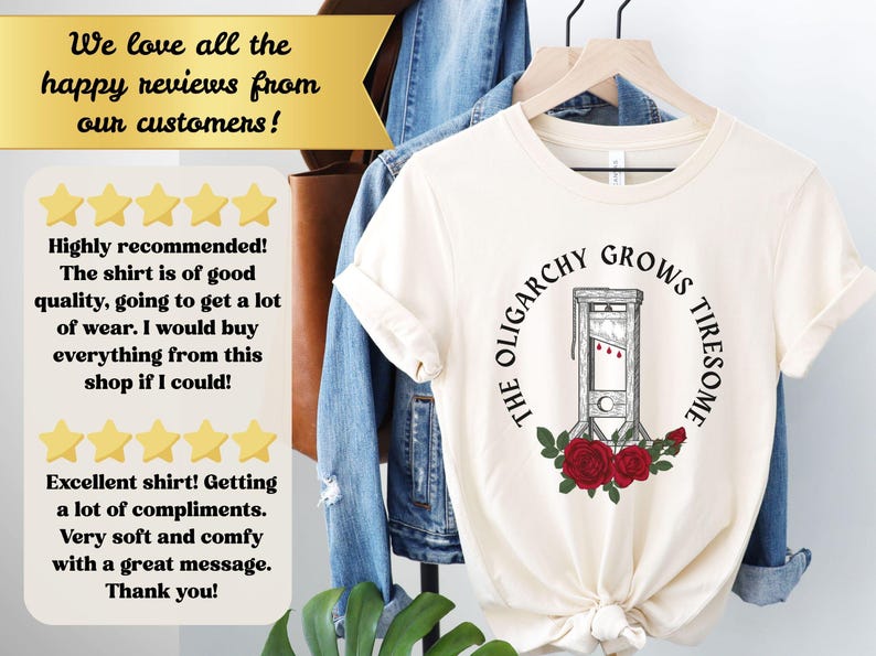 May include: Cream-colored t-shirt featuring a guillotine graphic with red roses and the text "THE OLIGARCHY GROWS TIRESOME." The shirt is hanging on a wooden hanger.