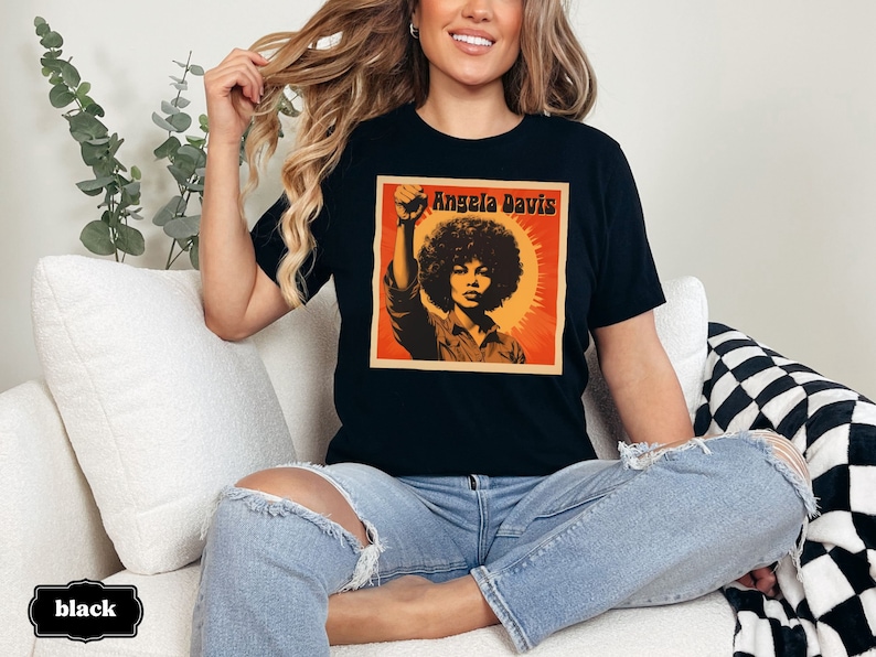 Pu&ograve; includere: Una maglietta nera con una grafica in stile vintage di Angela Davis con il testo "Angela Davis" stampato sul davanti.