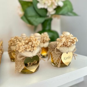 May include: Small glass jars filled with honey, decorated with burlap, dried flowers, and a gold heart-shaped tag with the name "Karlie" written on it.
