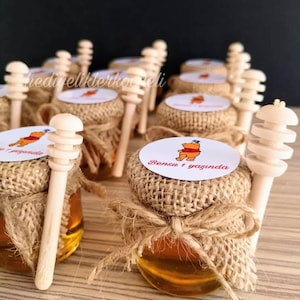 May include: Small glass jars filled with honey, each topped with a burlap lid and a wooden honey dipper. The jars are decorated with a Winnie the Pooh sticker that reads "Bensu 1 yaşında".
