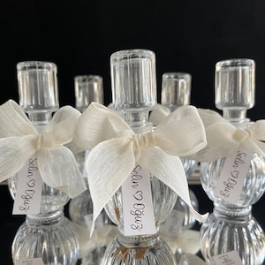May include: Set of clear glass bottles with a textured surface, tied with white ribbon bows and personalised tags that read "Selin & Oguz" in cursive.