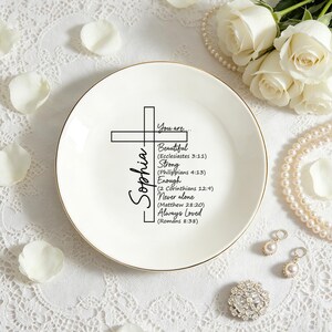 Può includere: Un piattino in ceramica bianca con bordo dorato, caratterizzato da una croce nera e dal testo: You are... Sophia, Beautiful (Ecclesiastes 3:11), Strong (Philippians 4:13), Enough (2 Corinthians 12:9), Never alone (Matthew 28:20), Always Loved (Romans 8:38).