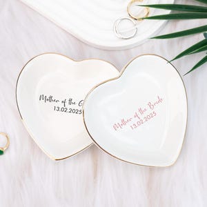 Puede incluir: Dos platos de cerámica en forma de corazón, blancos con borde dorado. El plato de la izquierda dice "Mother of the Groom 13.02.2025" y el plato de la derecha dice "Mother of the Bride 13.02.2025".