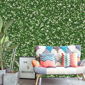 Könnte beinhalten: Ein weißes Sofa mit bunten, gemusterten Kissen steht vor einer grünen Wand, die mit kleinen weißen Blüten bedeckt ist. Ein gerahmtes Schild lautet "Sie ist schön".