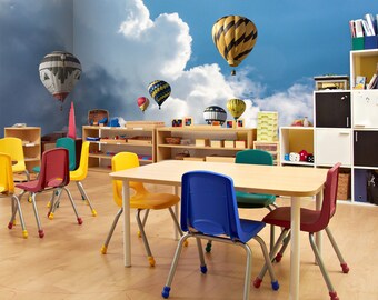 May include: A classroom setting with a colorful mural of hot air balloons against a blue sky with white clouds. The room has a table and chairs, and shelves with colorful toys.