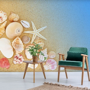 Könnte beinhalten: Ein grüner Samt-Sessel mit Holzrahmen steht vor einer Wandmalerei, die eine Strandszene mit Muscheln und einem Seestern darstellt. Ein kleiner Holztisch mit einer Topfpflanze steht vor dem Sessel.