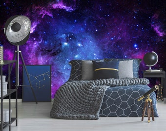 May include: A bedroom with a galaxy-themed wall mural featuring a nebula with blue and purple hues. The bed has a dark gray knitted blanket and a navy blue duvet with a geometric pattern. A telescope is on a wooden tripod next to the bed.
