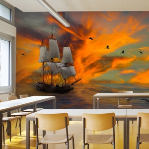 May include: A vintage sailing ship with white sails against a dramatic orange and yellow sunset sky. The ship is sailing on a calm sea with a few birds flying overhead.