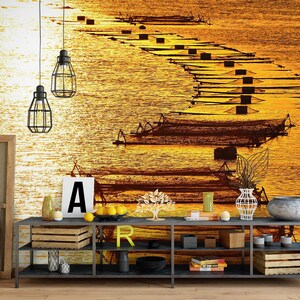 Könnte beinhalten: Ein schwarzes Metallregal mit drei Regalbrettern, auf denen verschiedene Gegenstände ausgestellt sind, darunter eine Holzkiste, Bücher und ein dekorativer Buchstabe 'R'. Das Regal steht vor einer Wand mit einem sonnenuntergangsfarbenen Bild von Fischernetzen im Wasser.