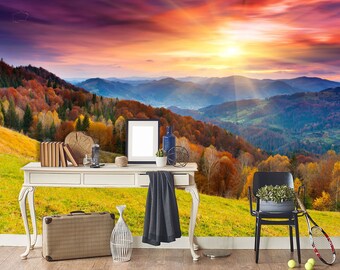 May include: A scenic wall mural depicting a vibrant sunset over a mountain range with colourful autumn foliage. The mural is displayed in a room with a white table, a suitcase, a picture frame, a black chair, and a tennis racket.