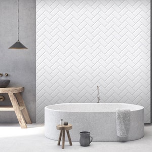 May include: A white freestanding bathtub with a gray concrete finish in a modern bathroom with a white herringbone tiled wall, a wooden stool, and a gray ceramic mug.