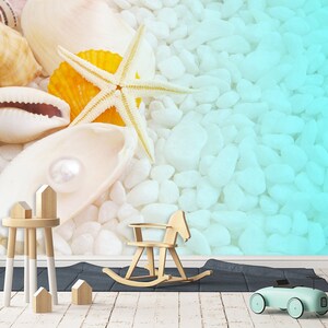 Puede incluir: Una concha blanca con una perla en su interior, una estrella de mar y otras conchas sobre un fondo de guijarros blancos. El fondo se desvanece a un color azul claro.