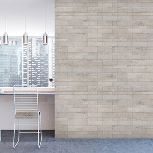 May include: A white kitchen with a bar counter and two white metal chairs. The wall behind the counter is made of light brown rectangular tiles. A window with a view of a city skyline is behind the counter.