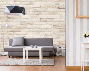 May include: A gray sofa with a gray pillow sits in front of a white brick wall. A white coffee table with two white cups sits in front of the sofa. A black geometric light fixture hangs from the ceiling. A white floor lamp is in the corner of the room.